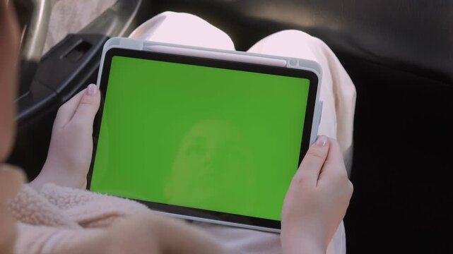 Person holds tablet with green screen inside car. Hands steady, focused on device. Suitable for travel, tech, or advertising concepts. Green screen ready for digital overlays