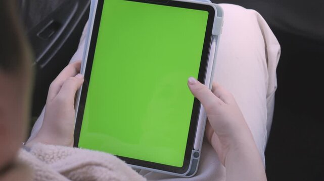 Close-up of hands holding tablet with green screen. Person seated inside car, focused on device. Ideal for app, software, or digital content promotion. Suitable for advertising, UI design