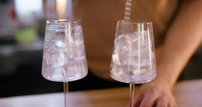 Preparing cocktail. Stirring ice. Bartender hand rotating frozen cube in stemmed glass on pub counter. Cooling for refreshing drink.