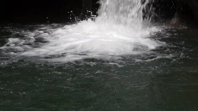 Close up static shot of a waterfall rushing into a clear river pool with splashing white foam 