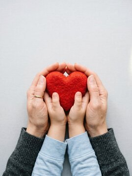 Red felt heart held in hands of parent and child, family love and support concept, healthcare and charity background