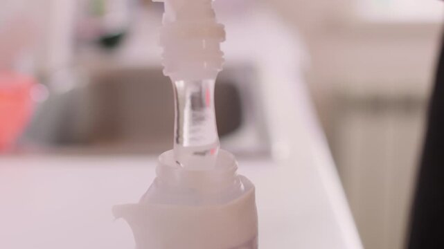 Dispensing thick product. Liquid serum. Beautician female hand pouring hyaluronic fluid transparent moisturizing acid in bottle for beauty procedure.