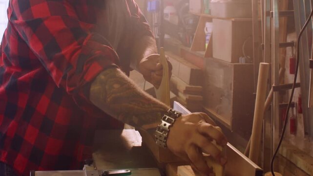 Carpentry occupation. Jointer machine. Male woodworker pushing plank with hand pad on professional industry power equipment in blur light.