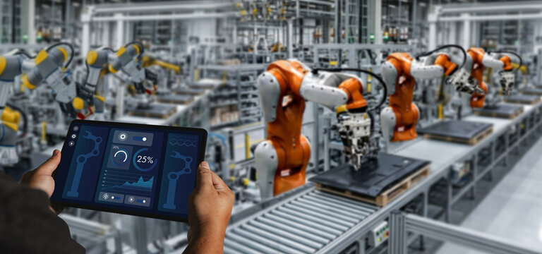 Person uses a tablet dashboard to monitor robotic automation on a factory assembly line, supporting manufacturing production control, data analysis, and industrial workflow management.
