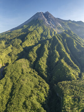 Aerial view of Mount Merapi, a majestic active volcano with lush green forested slopes and deep ravines in Sleman Regency, Special Region of Yogyakarta, Indonesia.