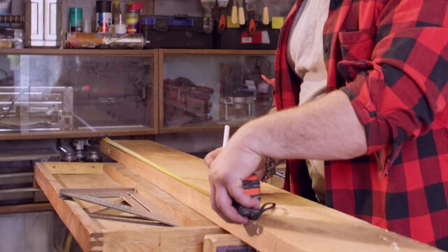 Woodworker service. Joinery production. Male carpenter with measuring tape try square marking pencil lumber plank in industry interior.
