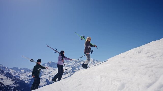 Cinematic shot of three skiers hiking uphill through snow while carrying skis in Verbier, Switzerland. The iconic Grand Combin dominates the background as the group ascends through the Swiss Alps duri