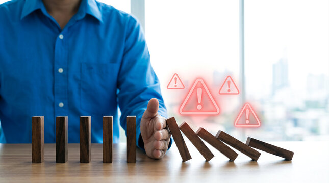 Businessman stopping falling wooden dominoes to prevent a chain reaction of business risks and financial crisis