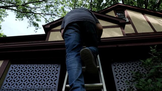 Man climbs ladder to clean his gutter of leaves and debris