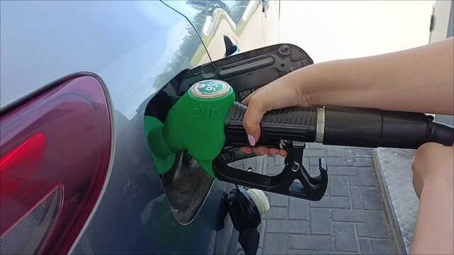 Close up of a woman refueling her modern car at a gas station, female driver filling petrol tank before road trip journey.