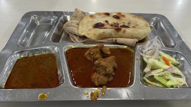 A comforting chicken thali platter featuring a rich, flavorful chicken curry served with soft, flaky parathas and a fresh side salad, India.