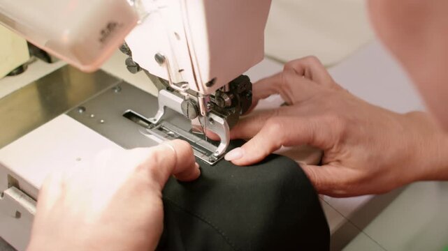 Tailor seam technique. Custom garment. Female seamstress hand stitching buttonhole on black clothes on professional industry machine.