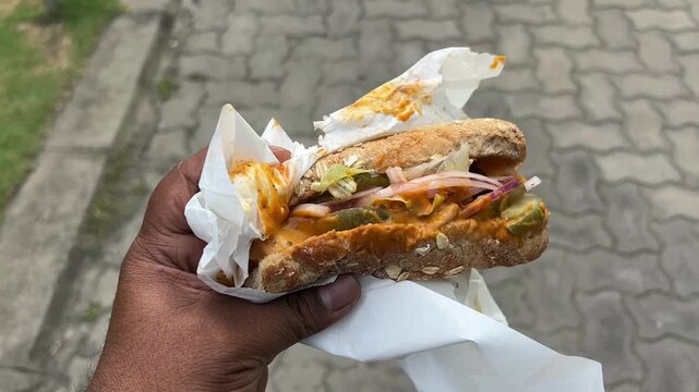 A close-up shot of a man holding a freshly loaded, gourmet submarine sandwich packed with crisp vegetables and premium meats, capturing a healthy fast-casual dining moment.
