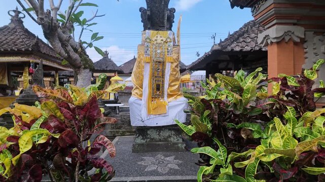 Traditional Balinese Hindu shrine wrapped in sacred yellow and white fabric called saput poleng inside a temple courtyard in Bali, Indonesia