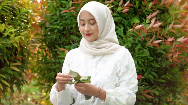 A young Asian Muslim woman is enjoying getuk pisang, a specialty food from Kediri, Indonesia, made from mashed steamed bananas wrapped in banana leaves.