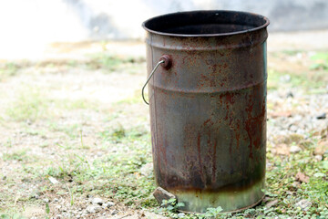 Fototapeta premium Rusty metal trash can standing outdoors on grassy ground, showcasing aged texture, corrosion, and industrial character in a natural environment