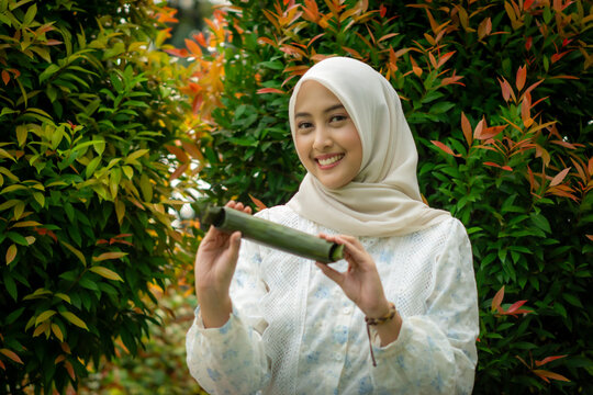 A young Asian Muslim woman is enjoying getuk pisang, a specialty food from Kediri, Indonesia, made from mashed steamed bananas wrapped in banana leaves.