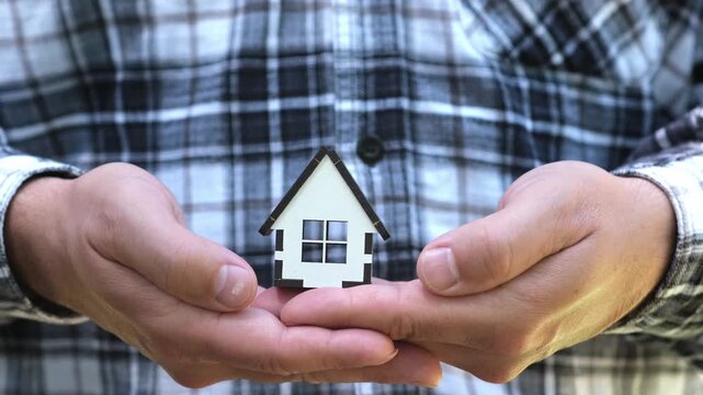 Miniature house in man hands outdoors. Home Insurance and real estate investment. Mortgage, home loan concept
