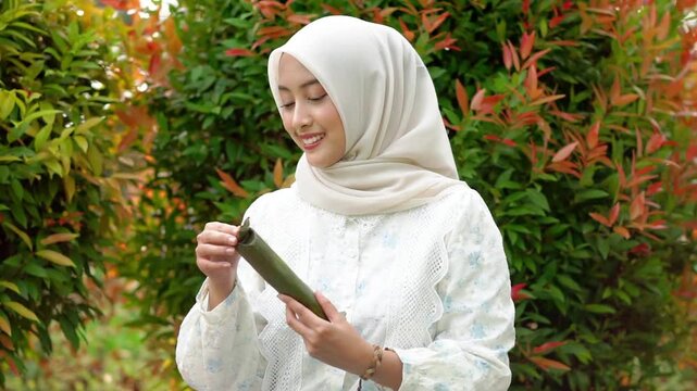 A young Asian Muslim woman is enjoying getuk pisang, a specialty food from Kediri, Indonesia, made from mashed steamed bananas wrapped in banana leaves.