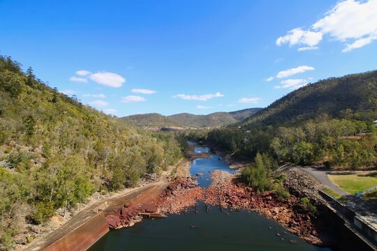 A beautiful high-angle view looking down at a rocky river winding through green hills under a bright blue sky at Somerset Dam in Queensland, Australia.