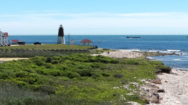 Point Judith Lighthouse alongside the US Coast Guard Station above coastal dunes and green marshland in Narragansett, capturing the maritime history of the Rhode Island coastline, aerial view