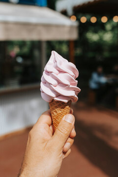 Close-up of a pink soft-serve ice cream cone held in hand.