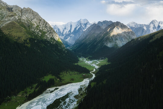 Aerial view of Boris Yeltsin Peak above the lush valley, with a winding glacial river, dense pine forests, and snow-capped mountains in Jety-Oguz, Issyk-Kul Region, Kyrgyzstan.