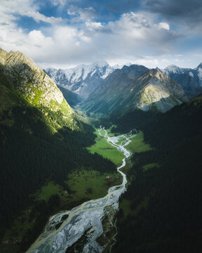 Aerial view of Boris Yeltsin Peak towering over the lush green valley with a winding river and dense coniferous forests in Jety-Oguz, Issyk-Kul Region, Kyrgyzstan.