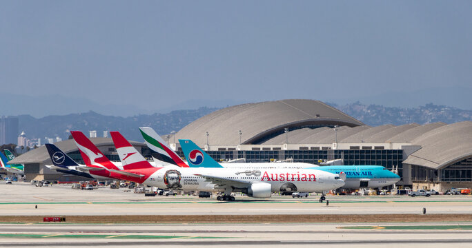 An Austrian Airlines Boeing 777-200 taking off with other widebody aircraft parked at gates in the background at Los Angeles International Airport (LAX) - Los Angeles, California, USA