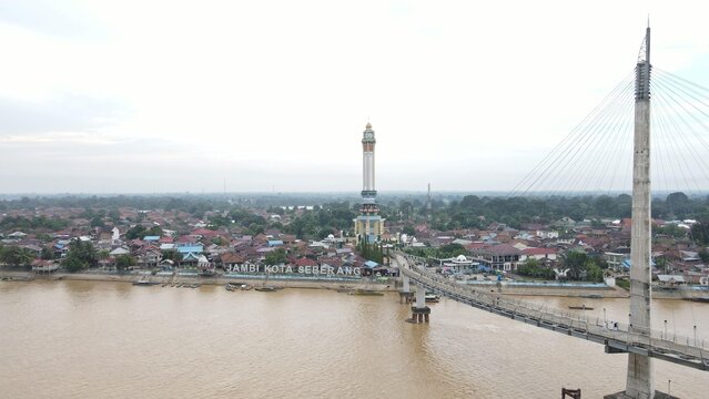 Aerial view of Jembatan Gentala Arasy spanning the Batang Hari River with the Jambi Kota Seberang district and historic rooftops in Kecamatan Jambi Timur, Jambi, Indonesia.
