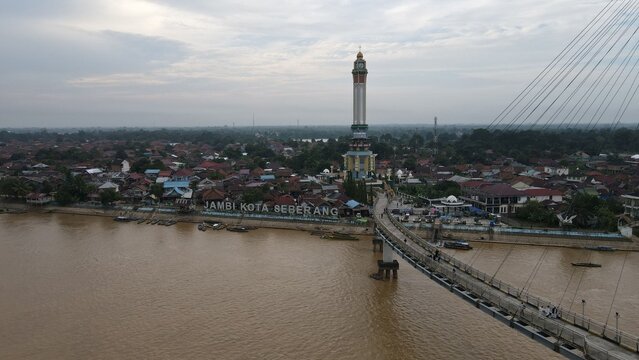 Aerial view of Jembatan Gentala Arasy spanning the Batang Hari river with the Jambi Kota Seberang clock tower in the background in Kecamatan Jambi Timur, Jambi, Indonesia.