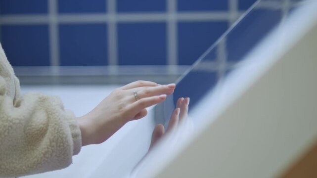 Person gently touches a glass surface. Background features blue tiled walls. Hand appears calm and curious. Scene suggests modern interior or architectural space. Good for design, travel