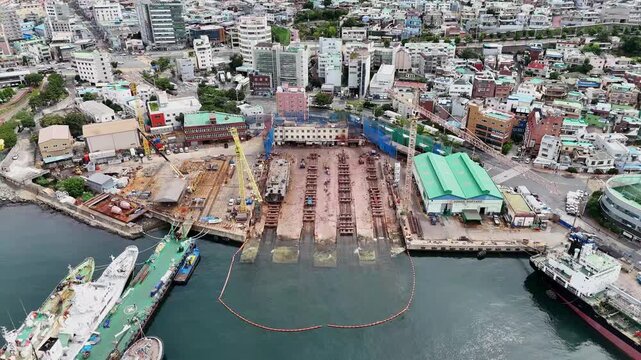Drone footage of a shipyard and dry dock construction site in Busan South Korea featuring docked vessels tower cranes shipbuilding facilities coastal industrial infrastructure