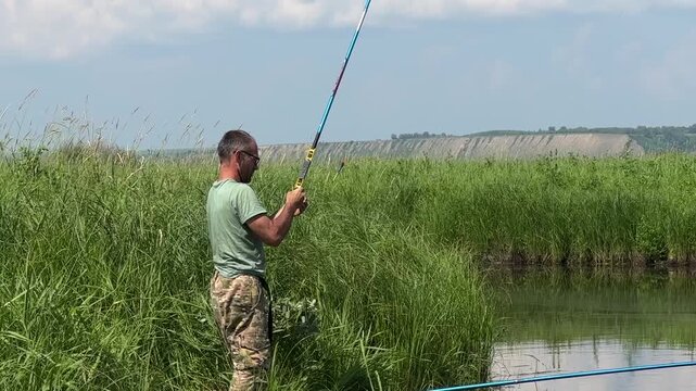 Close-up of fisherman holding fishing rod by the river, man angler focused on fishing, outdoor hobby and nature lifestyle, peaceful water and green bank.