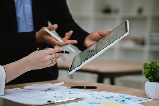 Two business people point to graphs and charts to analyze market data, balance sheet, account, net profit to plan new sales strategies to increase production capacity.