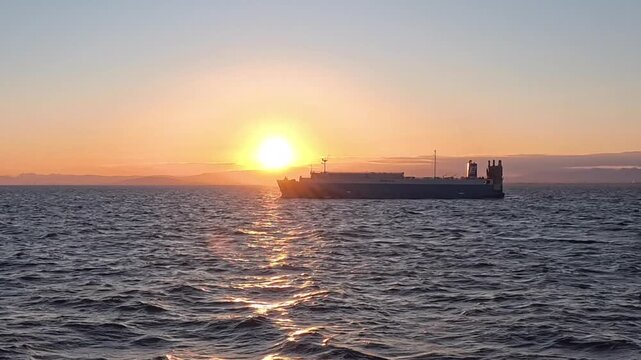 Large car carrier ship sailing nearby on the ocean against a vibrant sunset