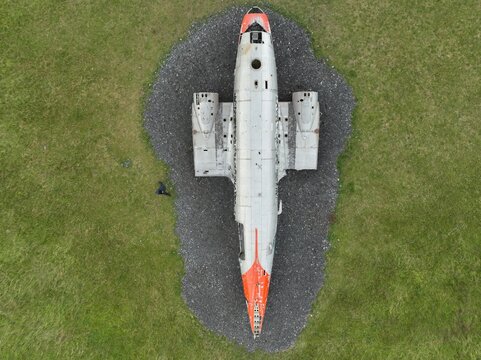 Aerial view of the DC-3 airplane wreck resting on a dark gravel patch surrounded by green grass in Hvolsvollur, Rangarthing eystra, Iceland.