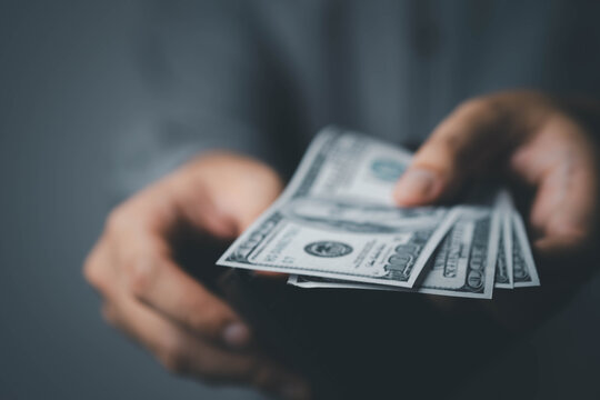 Close-up of hands holding and counting US dollar banknotes in a dark atmosphere, symbolizing cash payment, financial transaction, business profit, personal finance, economy and money exchange concepts
