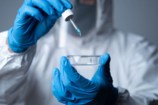 Scientist in protective suit using dropper and petri dish for laboratory research, medical testing, representing biotechnology, pharmaceutical development, healthcare innovation, scientific analysis.