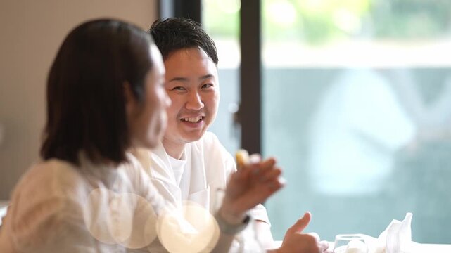 Soft light filters through a cafe window. Two people sit close, engaged in quiet conversation. One rests a hand near their mouth, listening intently. The other gestures gently, sharing thoughts