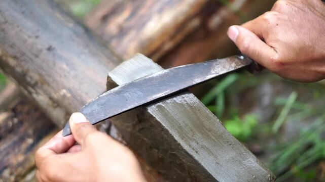Close-up shot of a man's hands sharpening a traditional kitchen knife blade using a wet natural whetstone on a wooden block.