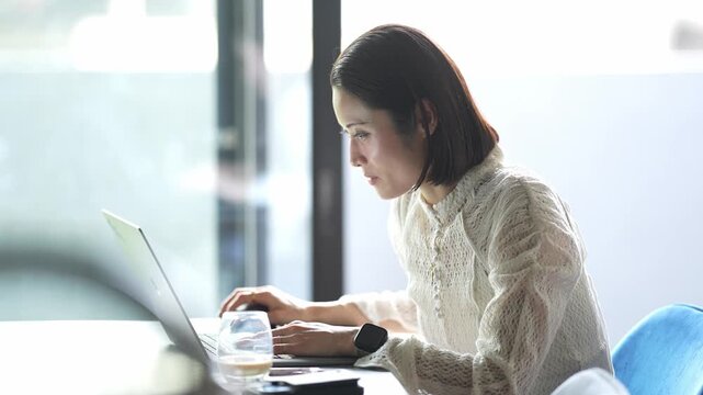 Soft sunlight illuminates a focused woman. She types on a laptop with quiet concentration. Her hands move steadily over the keyboard. The room holds calm, professional energy
