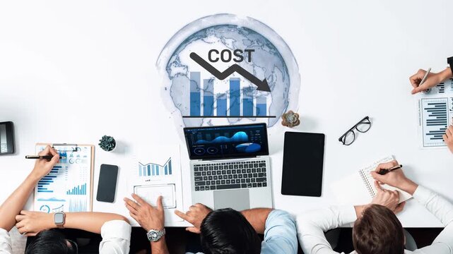 A business team collaborates on global economic analysis, focusing on cost reduction strategies. Laptops, notebooks, and graphs illustrate their data-driven approach. Raster