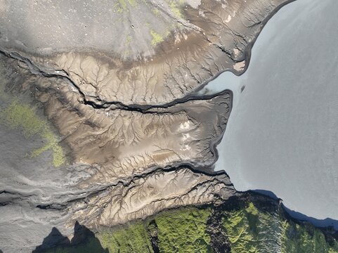 Aerial view of intricate glacial river sediment patterns and mossy volcanic terrain near the water in Kirkjubaejaklaustur, Skaftarhreppur, Iceland.