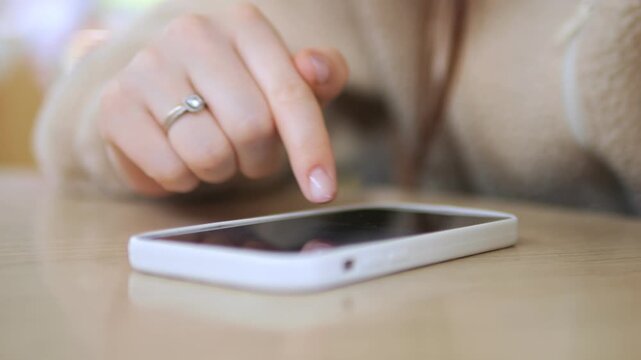 Hand with a ring taps a white smartphone on a wooden surface. The person seems calm and focused. Ideal for tech, communication, or daily routine themes. Suitable for websites, ads
