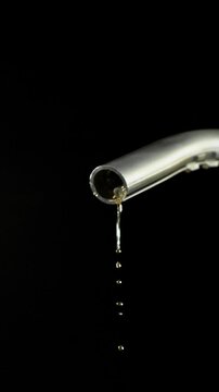 Super slow motion (1000 fps) fuel drops dripping from gasoline nozzle, symbol of depletion and fuel shortage. Minimal liquid flow on black background, dramatic lighting, energy crisis concept.
