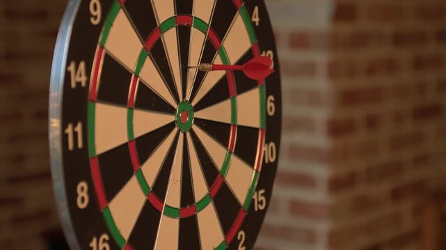 A close-up of a dartboard mounted on a brick wall with colorful segments and numbered rings in warm indoor lighting.