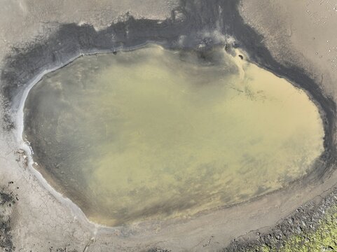 Aerial view of the Langisjor campsite pond featuring light-colored water set against dark volcanic soil and rugged terrain in Kirkjubaejaklaustur, Skaftarhreppur, Iceland.