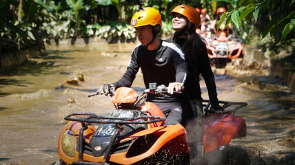 Young couple riding an ATV through tropical jungle trails and muddy puddles. Exciting outdoor adventure featuring quad biking, nature exploration, extreme travel and active lifestyle in a scenic envir © DR26