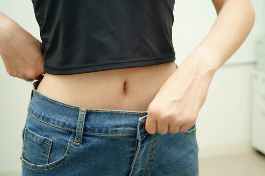Young Asian woman losing weight wearing loose pants in oversize jeans.